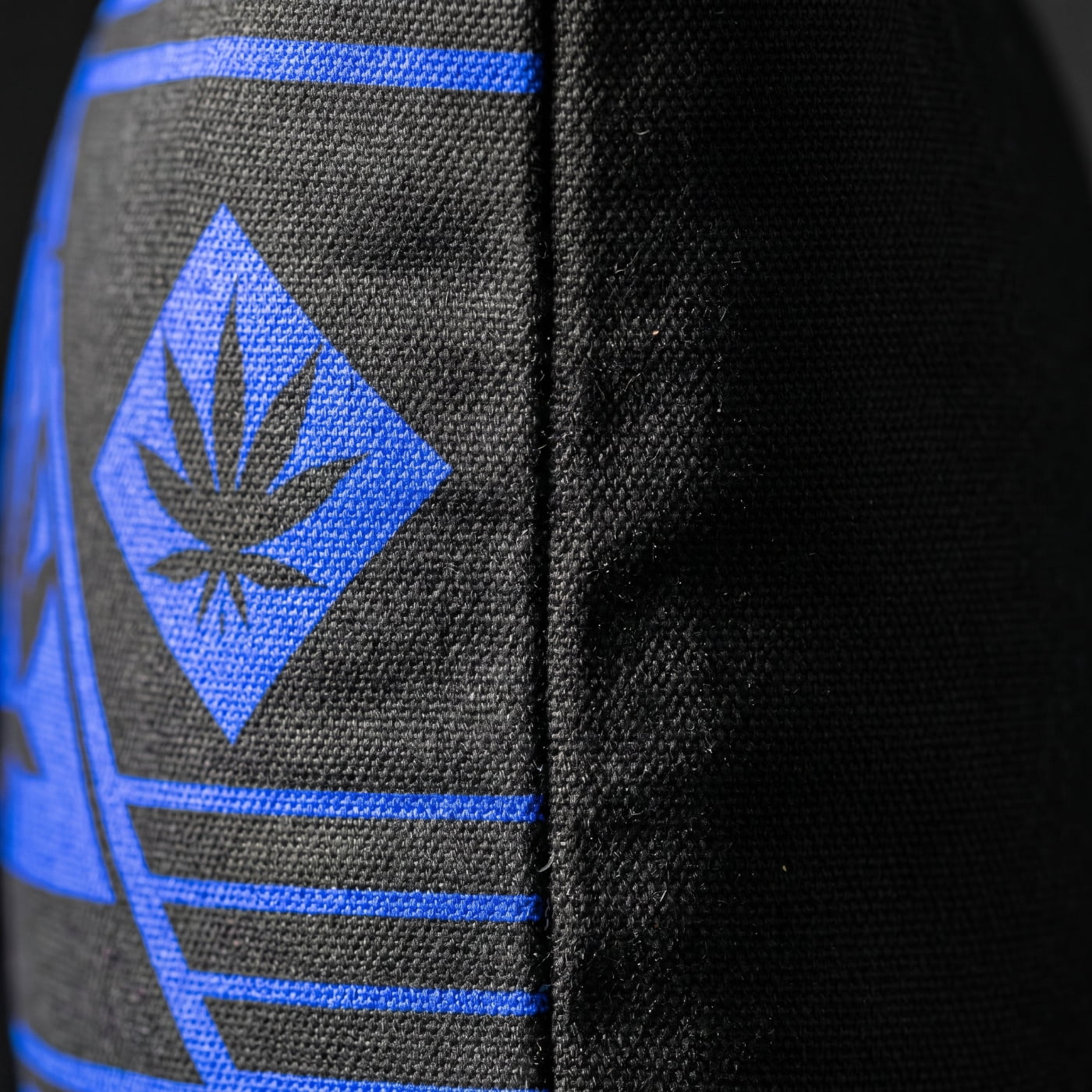 Side-angle detail of the NGU Architect pillow showcasing the thick 275gsm canvas texture and the vector-sharp blue graphic alignment on the matte-black fabric.