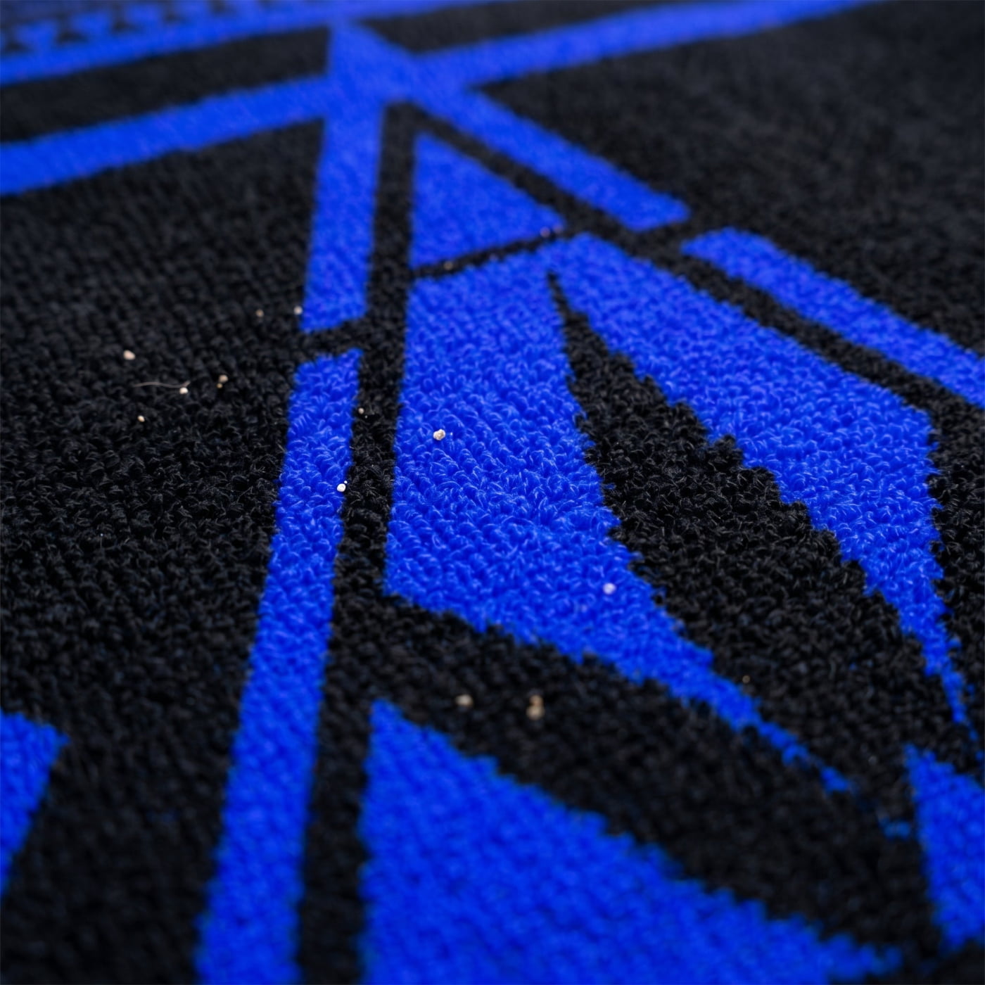 Macro close-up of the Black and Electric Blue NGU Architect Towel. The shot highlights the high-density 360gsm cotton loops and the sharp, vector-clear Electric Blue geometric design. Hard rim lighting emphasizes the material depth and premium fabric weave